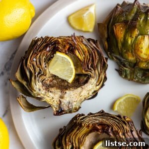 Four air-fried artichoke halves on a large plate, one cut side down and the others cut side up, all crispy and garnished with lemon slices.