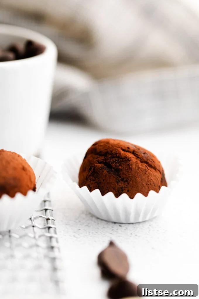 Amaretto Dream Truffles 3 Close-up of a velvety chocolate truffle, lightly dusted with cocoa powder, nestled in a small cupcake liner. Other truffles are visible in the soft background.