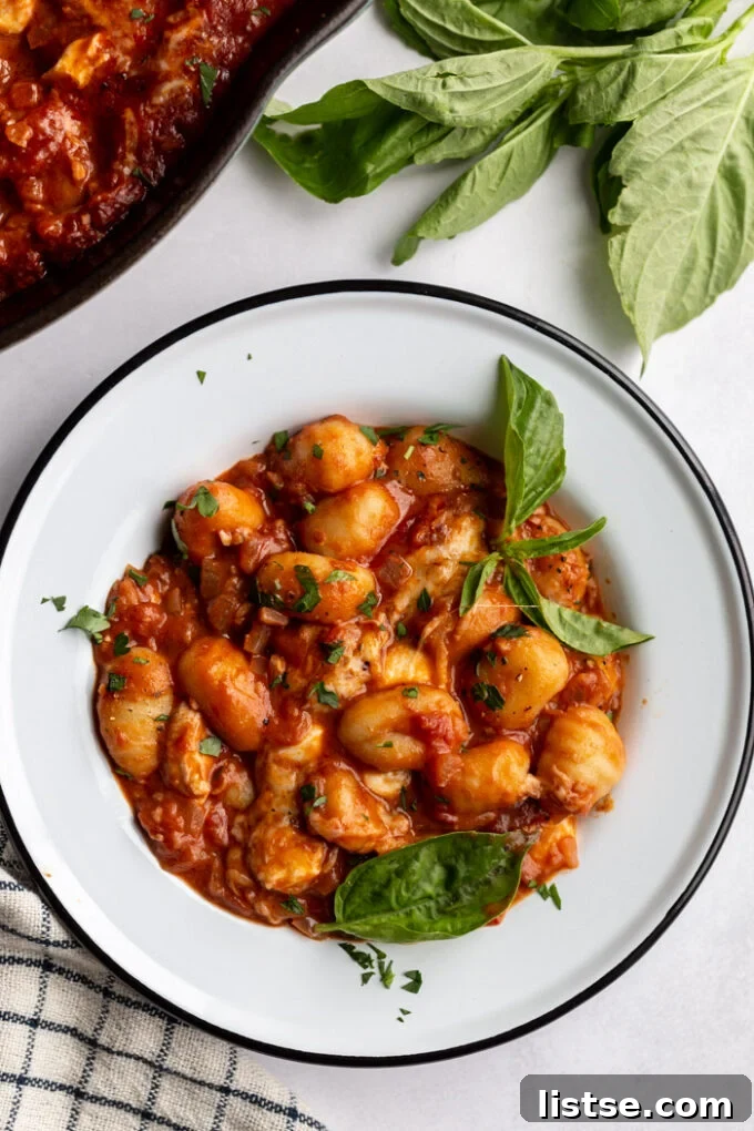 Sun Ripened Tomato Gnocchi 3 tomato sauce gnocchi in a white bowl with fresh herbs and a skillet in the corner