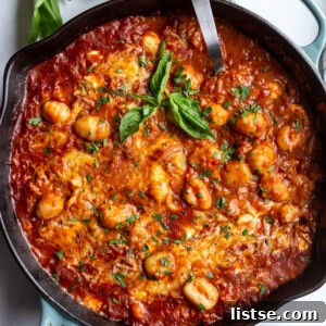 skillet with tomato sauce and gnocchi covered with cheese and garnished with fresh basil. spoon sticking out the side
