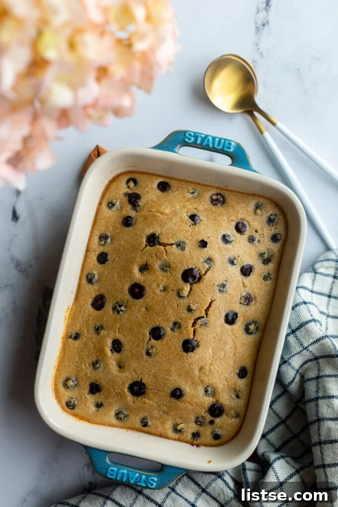 Baked Oats Double the Delight 4 baked oats with blueberries in a small casserole dish with a napkin and spoons on the side. pink flowers in the corner of the shot