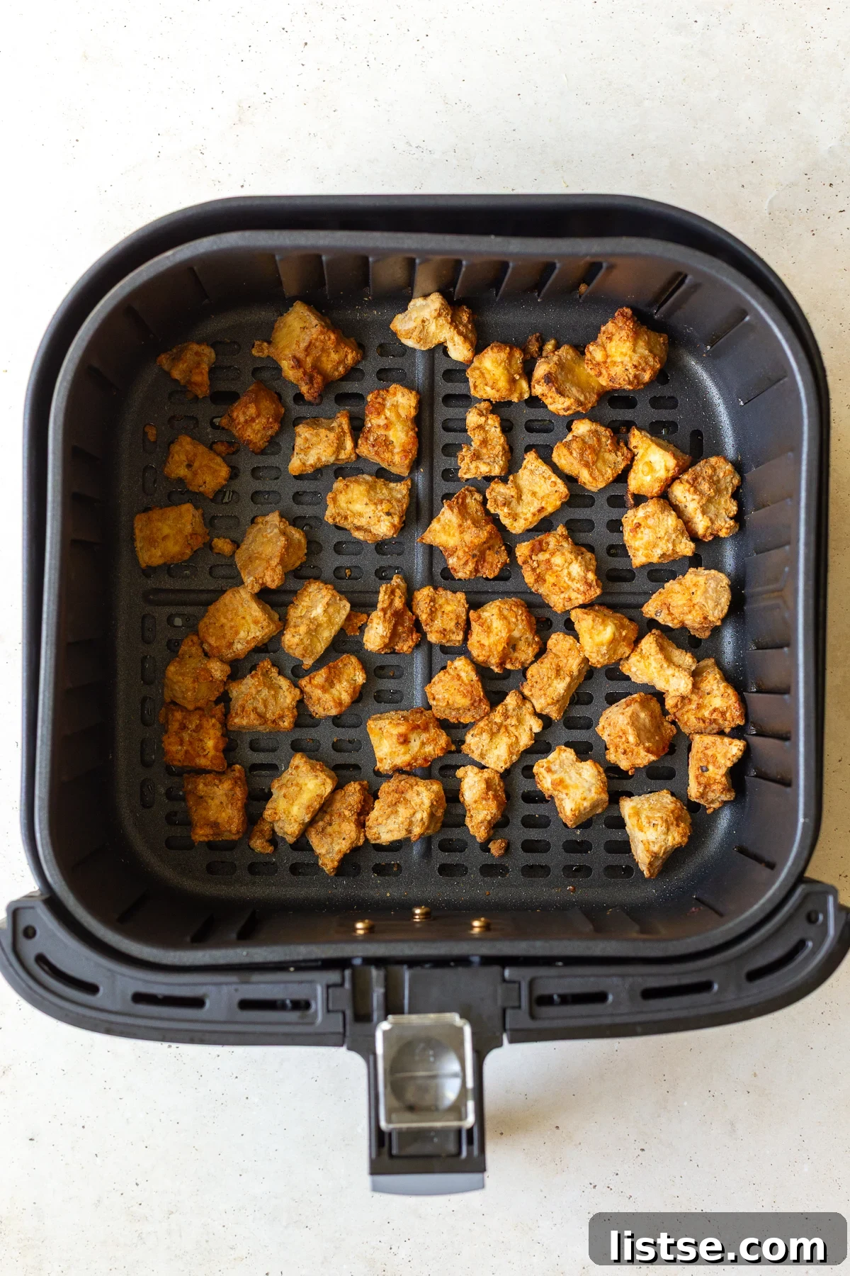 Tofu pieces neatly arranged in an air fryer basket, ready for cooking.