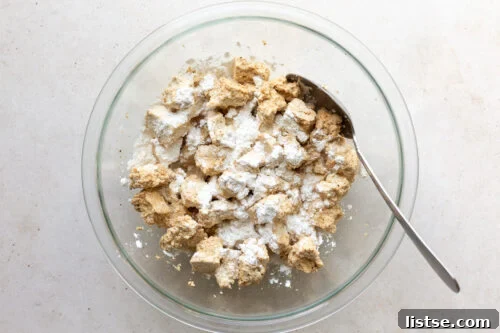 Tofu torn into chunks and tossed with soy sauce and cornstarch in a large bowl, showing the coating process.