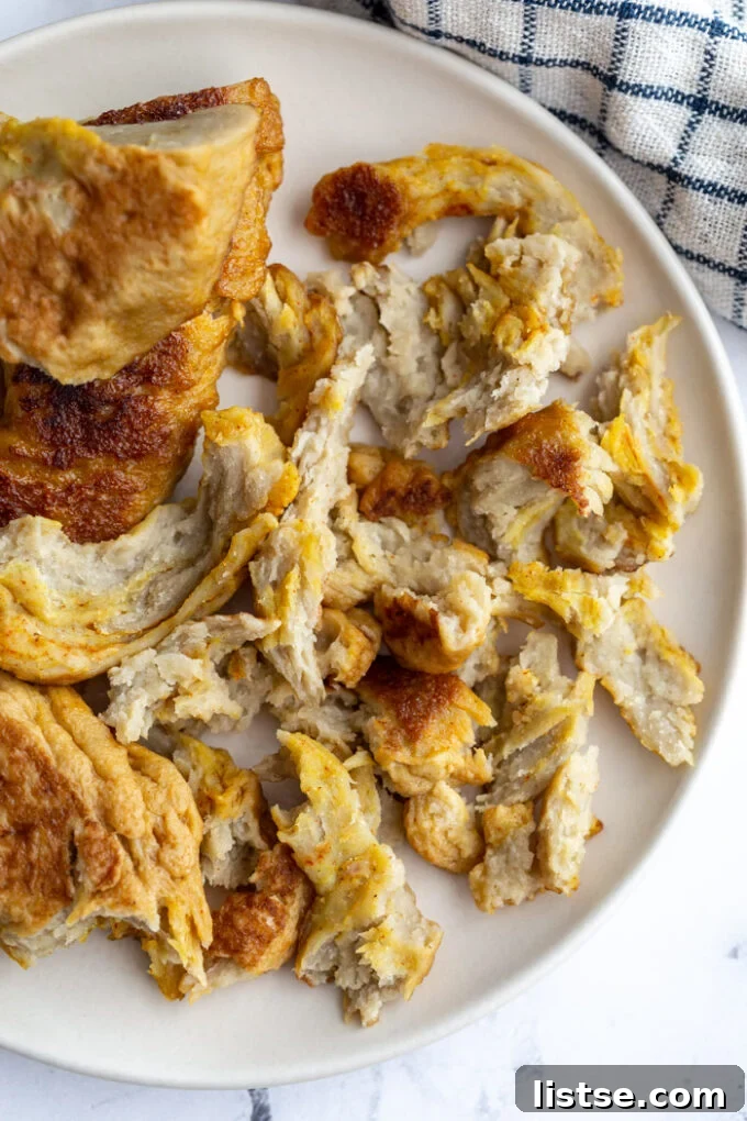 Viral Seitan Sensation 3 Shredded seitan resembling chicken, served on a white plate with a kitchen towel in the background, highlighting its fibrous, pull-apart quality.