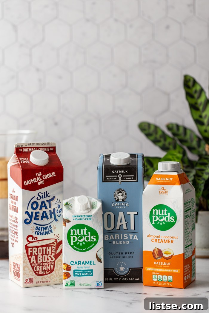 Four different brands of vegan coffee creamer bottles lined up on a kitchen counter next to a plant and a Chemex coffee maker, against a tile backdrop.