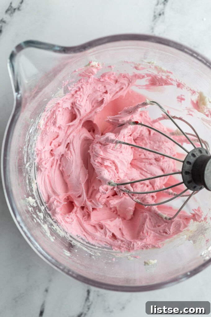 Freshly mixed light pink sugar cookie frosting in a stand mixer, demonstrating perfect consistency.