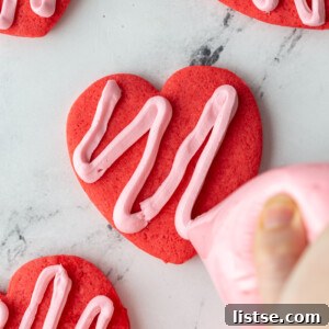 red heart cookie being frosted with pink frosting