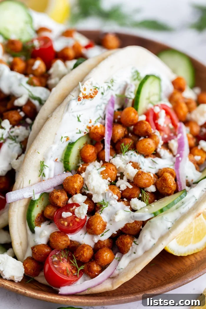 Effortless Vegan Chickpea Gyros 2 gyro made with crispy chickeas topped with red onion and feta cheese. on a wood plate