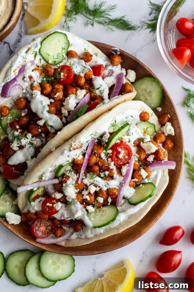 Effortless Vegan Chickpea Gyros 3 gyro made with crispy chickeas topped with red onion and feta cheese. on a wood plate