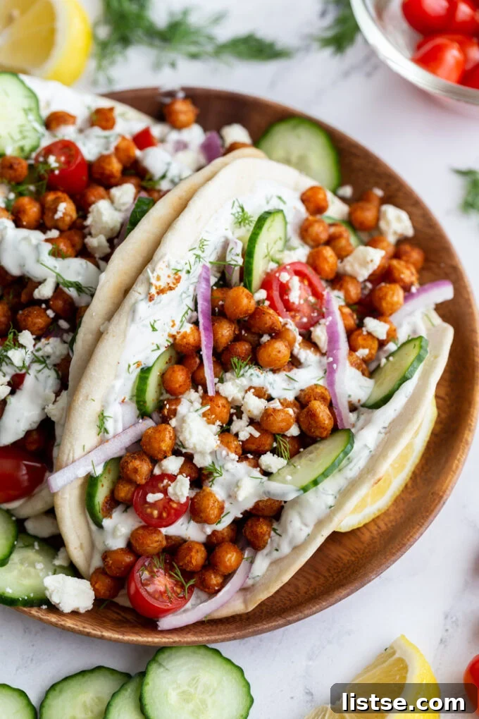 Effortless Vegan Chickpea Gyros 5 gyro made with crispy chickeas topped with red onion and feta cheese. on a wood plate