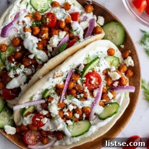 Effortless Vegan Chickpea Gyros 6 gyro made with crispy chickeas topped with red onion and feta cheese. on a wood plate