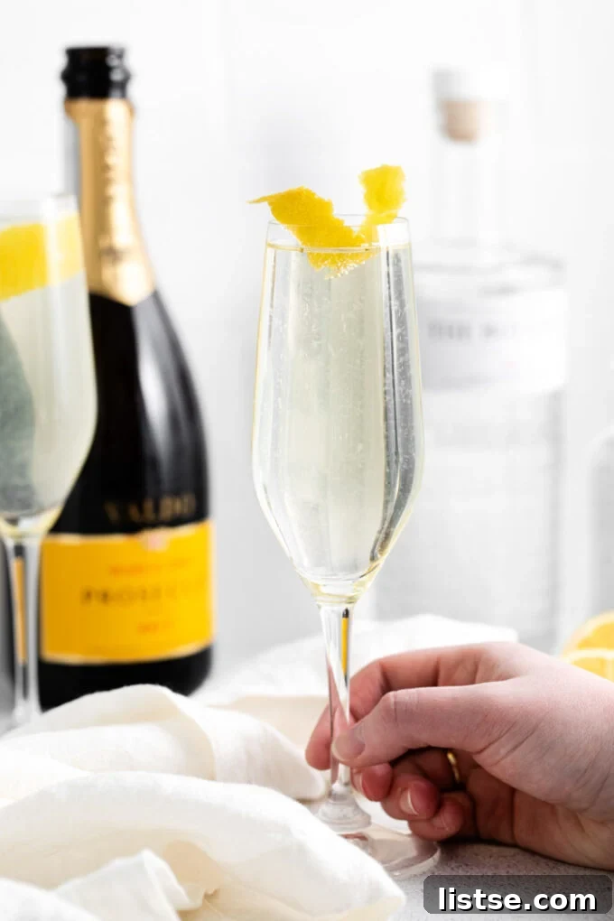Hand holding a sparkling French 75 Cocktail in a champagne flute with a lemon twist