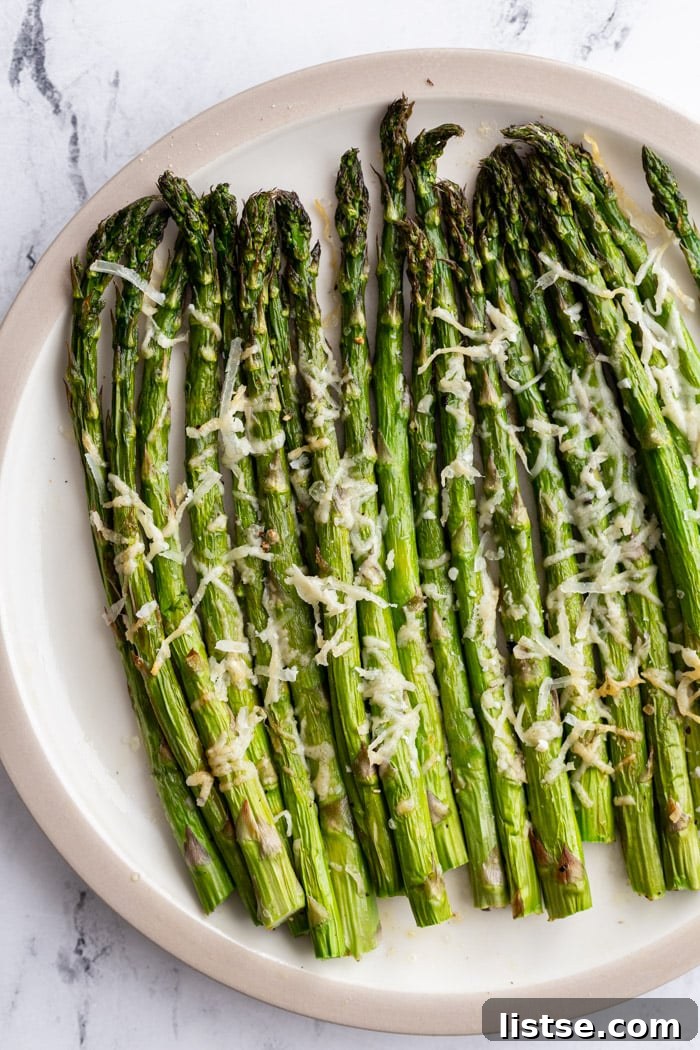 Crispy air fryer asparagus topped with freshly grated parmesan cheese on a white serving plate