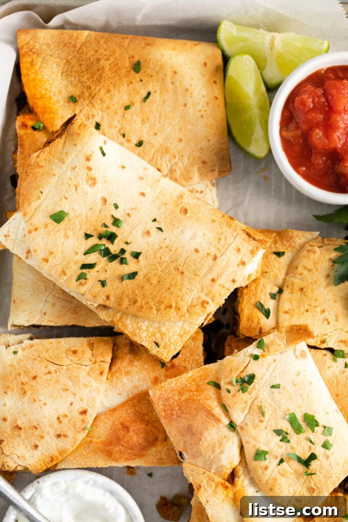 Fully assembled sheet pan quesadilla with a top layer of tortillas and folded edges, ready for baking, surrounded by garnishes.
