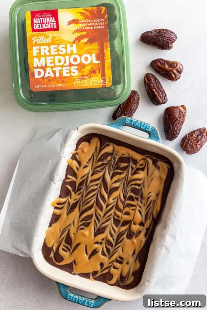 pan filled with date bars that are covered in chocolate and peanut butter drizzle. a green carton of natural delights medjool dates in the frame