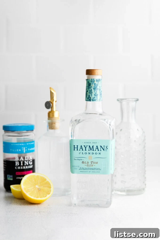 ingredients in front of a white background for tom collins: gin, lemon, cherries, simple syrup, and club soda