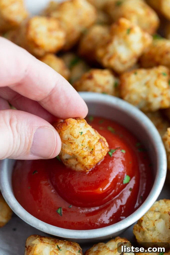 hand dipping a tater tot into a small bowl of ketchup with more tater tots in the background