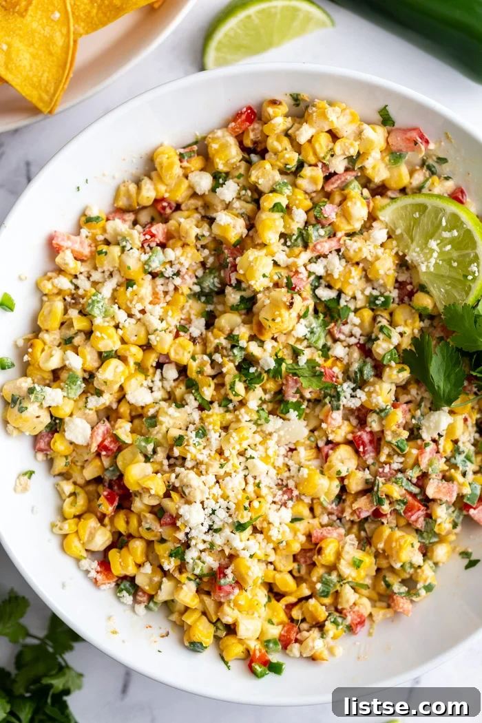 Creamy Mexican Street Corn Salad 2 Large white bowl of Mexican Street Corn Salad, Esquites, garnished with cotija cheese, fresh cilantro, and a lime wedge. The scene suggests a fresh and delicious summer dish.