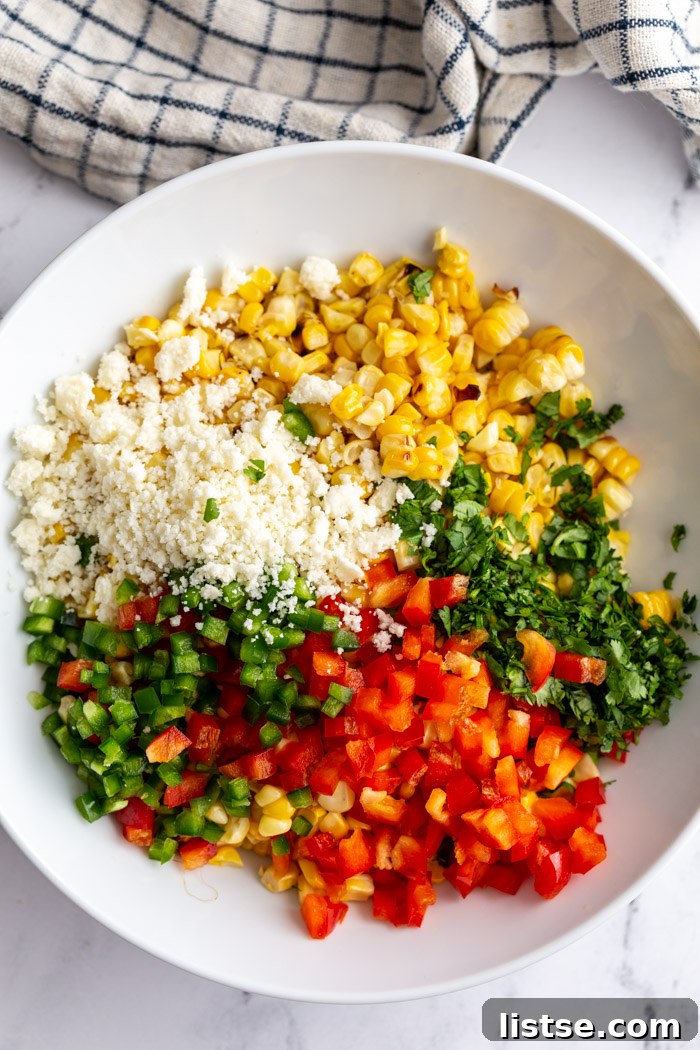 Creamy Mexican Street Corn Salad 4 A collection of fresh ingredients laid out in a large bowl, including golden grilled corn kernels, crumbled cotija cheese, vibrant cilantro, crisp bell pepper, and a kick of jalapeño, all ready to be mixed into the Mexican Street Corn Salad.