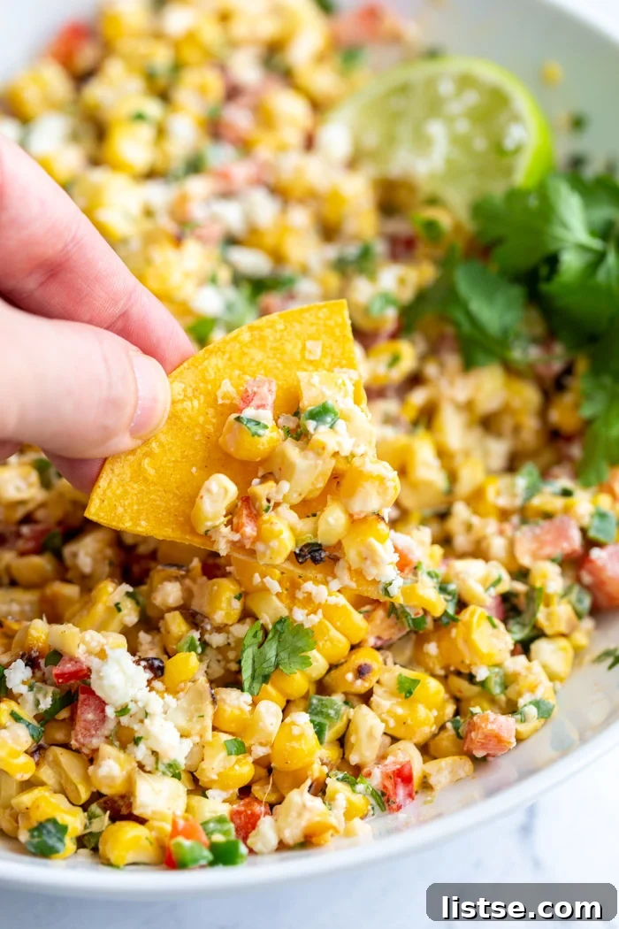 Creamy Mexican Street Corn Salad 5 A hand holds a tortilla chip, scooping a generous portion of the Mexican Street Corn Salad from a large white bowl, highlighting its perfect texture for dipping and enjoying.