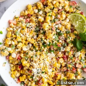 Large white bowl of Mexican Street Corn Salad topped with cotija cheese and a lime with cilantro in the scene