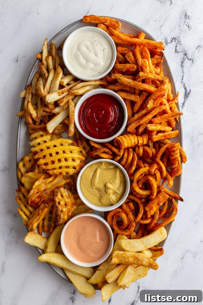 Large tray filled with various kinds of perfectly air-fried french fries, accompanied by four different dips in small ramekins, showcasing a delicious spread for a snack or party.