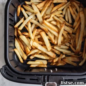 black basket of an air fryer with cooked frozen french fries in it