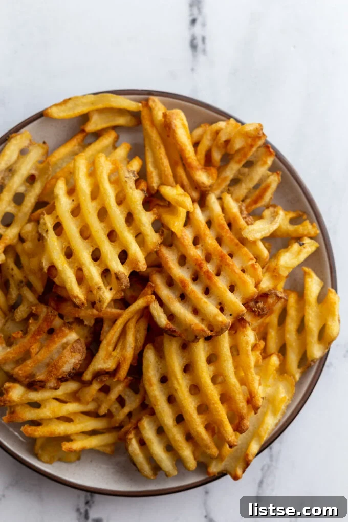 A simple white plate generously piled with golden, perfectly cooked waffle fries, showing off their signature criss-cross pattern and crispy edges.