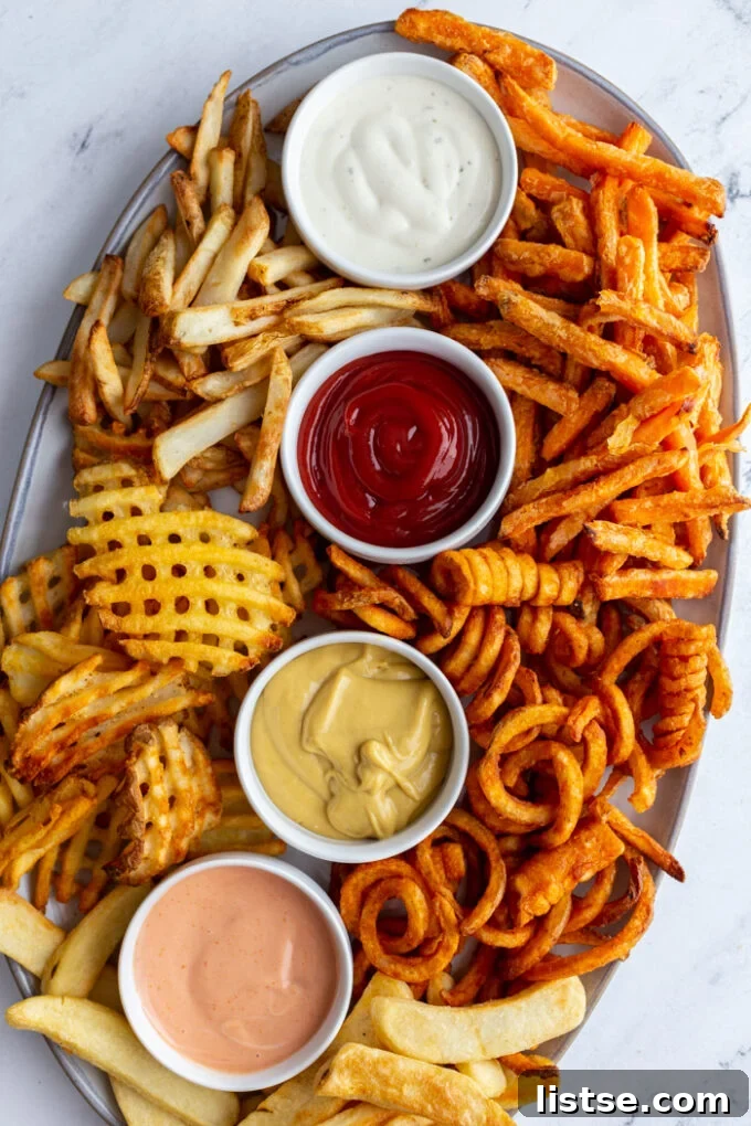 A large and appealing charcuterie-style tray loaded with a variety of air-fried french fries, including regular, curly, waffle, and steak fries, presented with four distinct dipping sauces in small dishes.