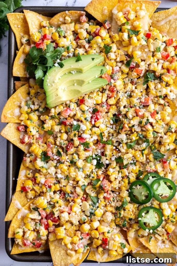 Elote Nachos 4 A close-up shot of a baking tray featuring a vibrant spread of Street Corn Nachos, artfully garnished with fresh cilantro and a couple of lime wedges, ready to be served.