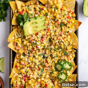 baking tray filled with nachos covered in mexican street cron. cilantro and limes in the corn of the shot