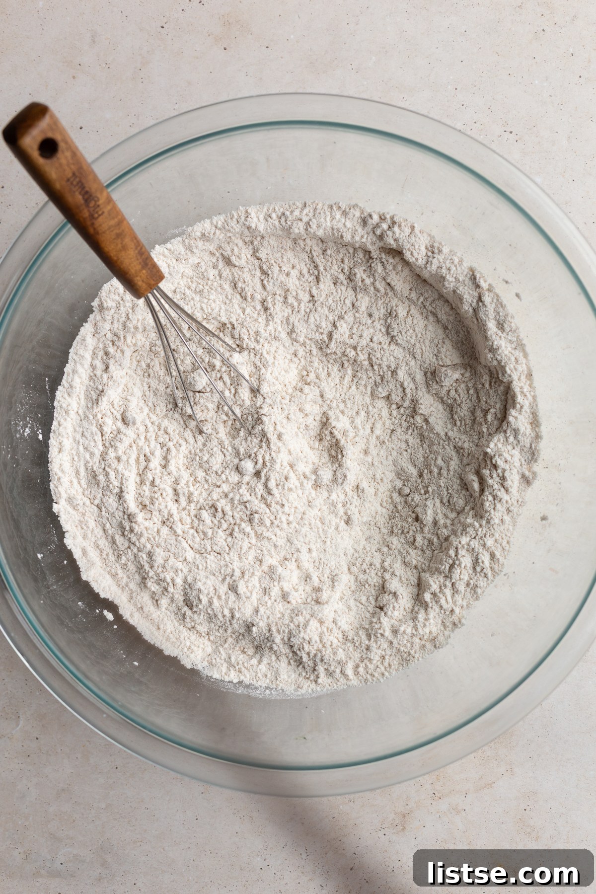 A whisk blending together all-purpose flour, baking powder, and brown sugar in a large mixing bowl.