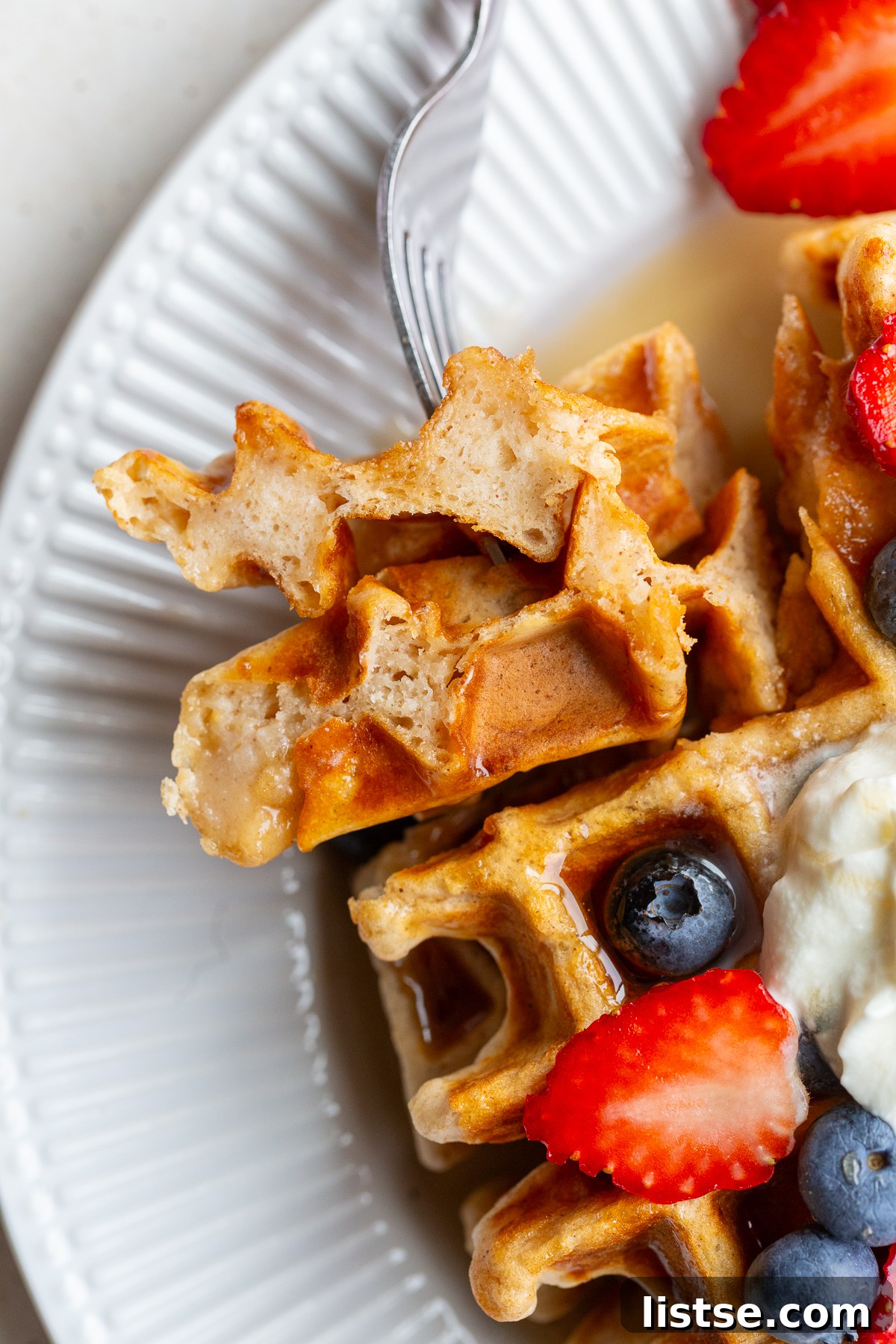 A perfectly golden vegan waffle held on a fork, adorned with vibrant fresh berries, ready for a delicious bite.