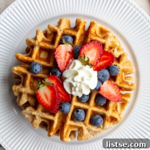 Waffle on a white plate topped with berries and whipped cream.