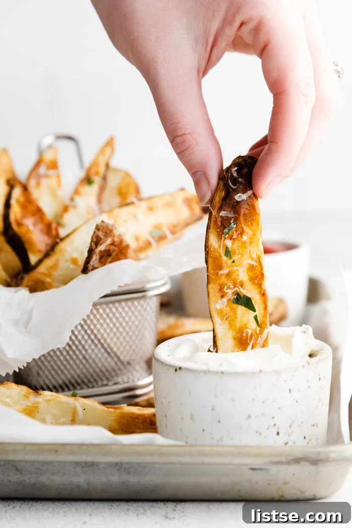 Hand dipping a golden-brown air fryer potato wedge into a small bowl of ranch dressing
