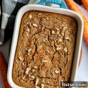 Green casserole dish filled with baked carrot cake oatmeal, with fresh carrots and a towel on the side.