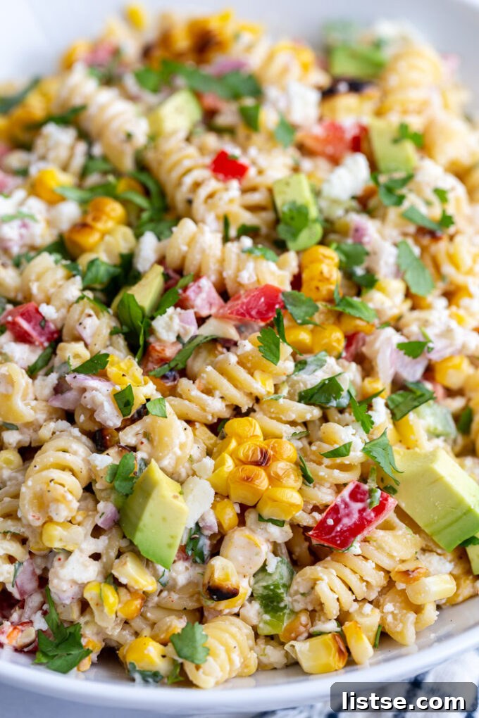 Vibrant Elote Pasta Salad 3 Close-up of vibrant Mexican Street Corn Pasta Salad made with rotini pasta, showcasing the rich crema dressing coating every ingredient, studded with bright yellow corn kernels, red bell peppers, and fresh cilantro, with crumbled cotija cheese visible.