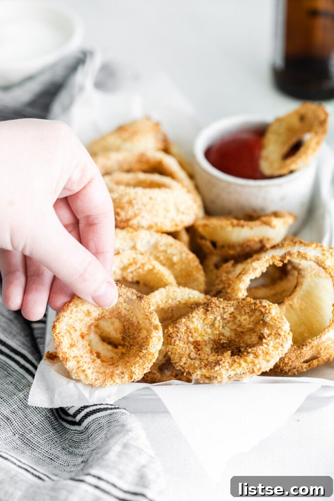 A hand reaching to grab a perfectly cooked air fryer onion ring from a plate.