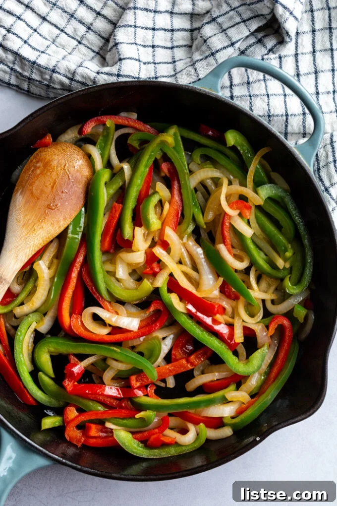 green + red bell peppers and onion being sauteed in a large cast iron skillet