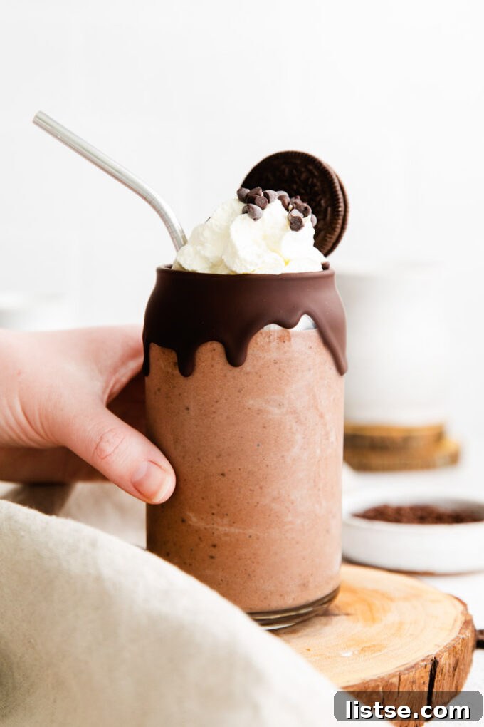Hand holding a cold glass with a chocolate vegan milkshake, topped with whipped cream and chocolate chips