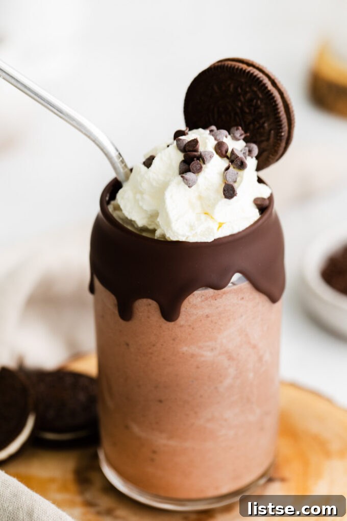 Chocolate milkshake topped with whipped cream, chocolate chips and an Oreo cookie, served in a tall glass