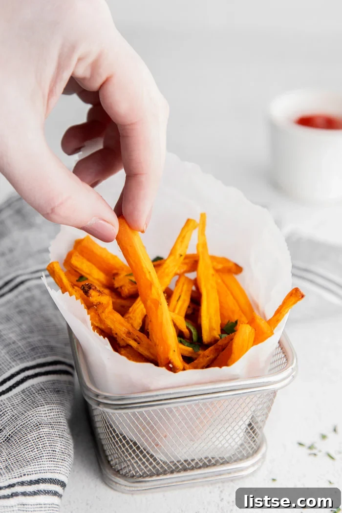 White hand picking up a golden-brown carrot fry from a rustic basket filled with perfectly cooked air fryer carrot fries.