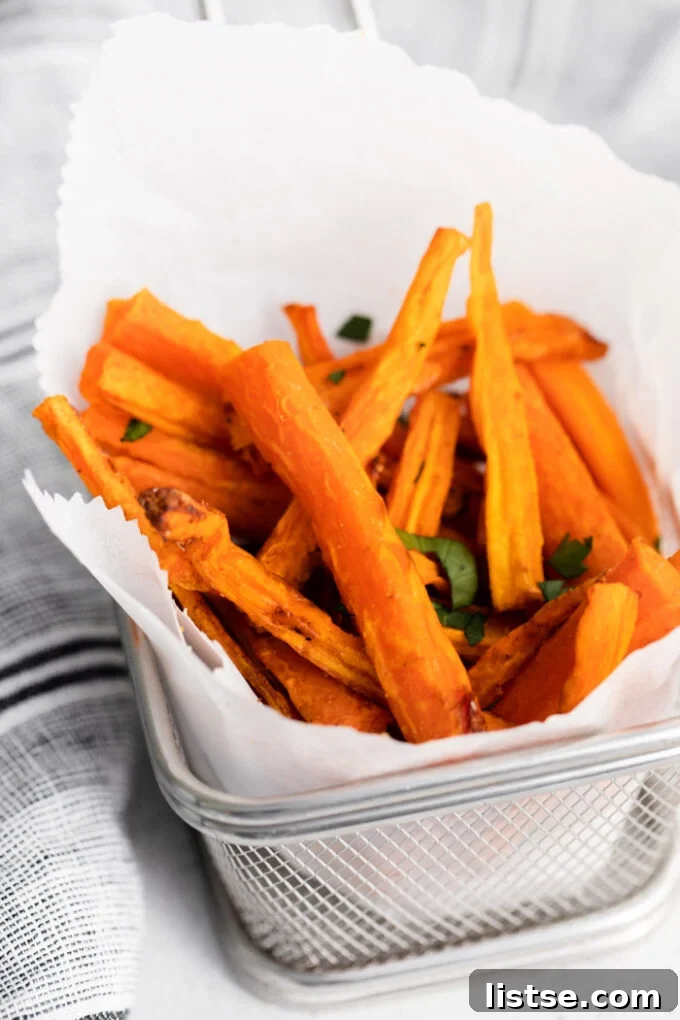 A basket lined with parchment paper, overflowing with golden-brown air fryer carrot fries, generously sprinkled with fresh green herbs.