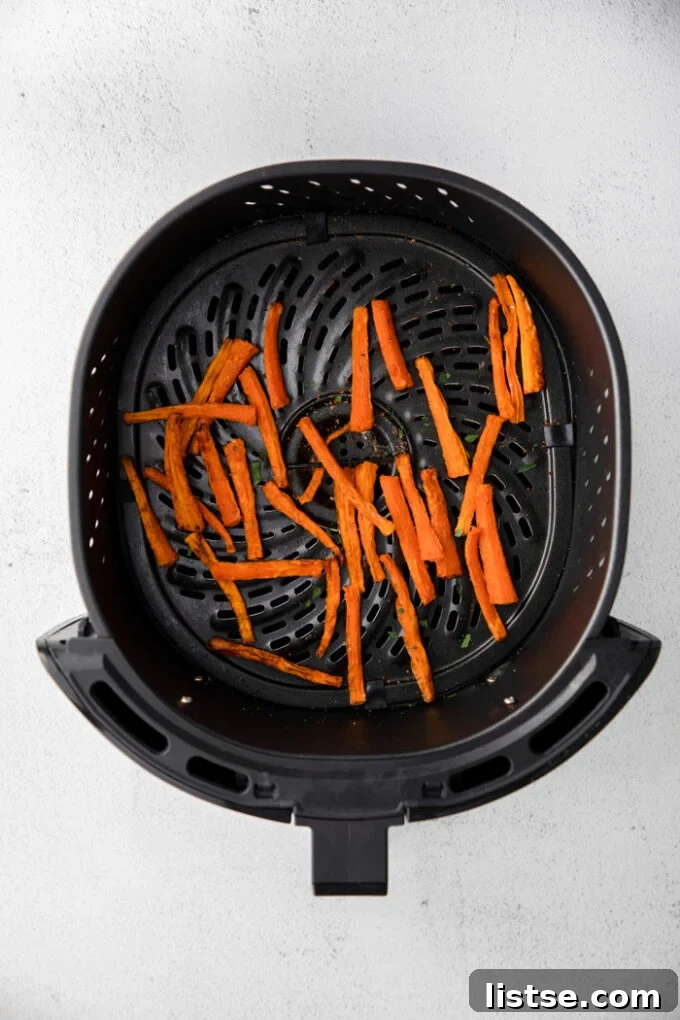 Close-up shot of crispy, golden-brown carrot fries inside an air fryer basket, showing their perfectly cooked texture.