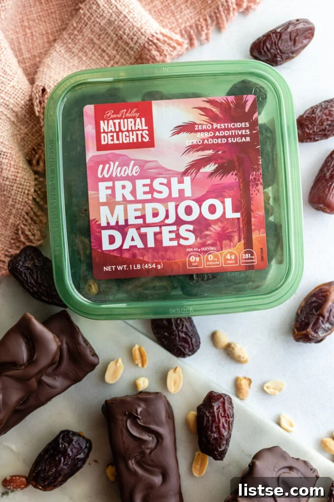 Homemade Snickers bars stacked next to a container of fresh Natural Delights Medjool dates, highlighting the key ingredient.