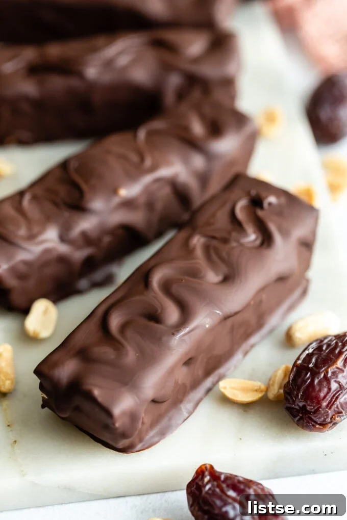 A selection of homemade Snickers candy bars surrounded by loose peanuts and Medjool dates, illustrating the core ingredients.