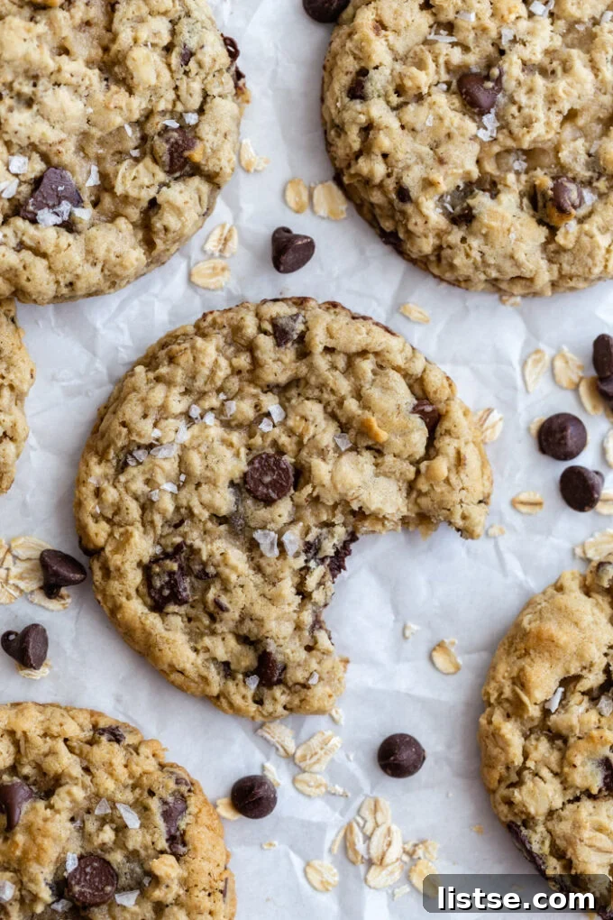 Chocolate chip oatmeal cookies on parchment paper with oats and chocolate chips scattered around