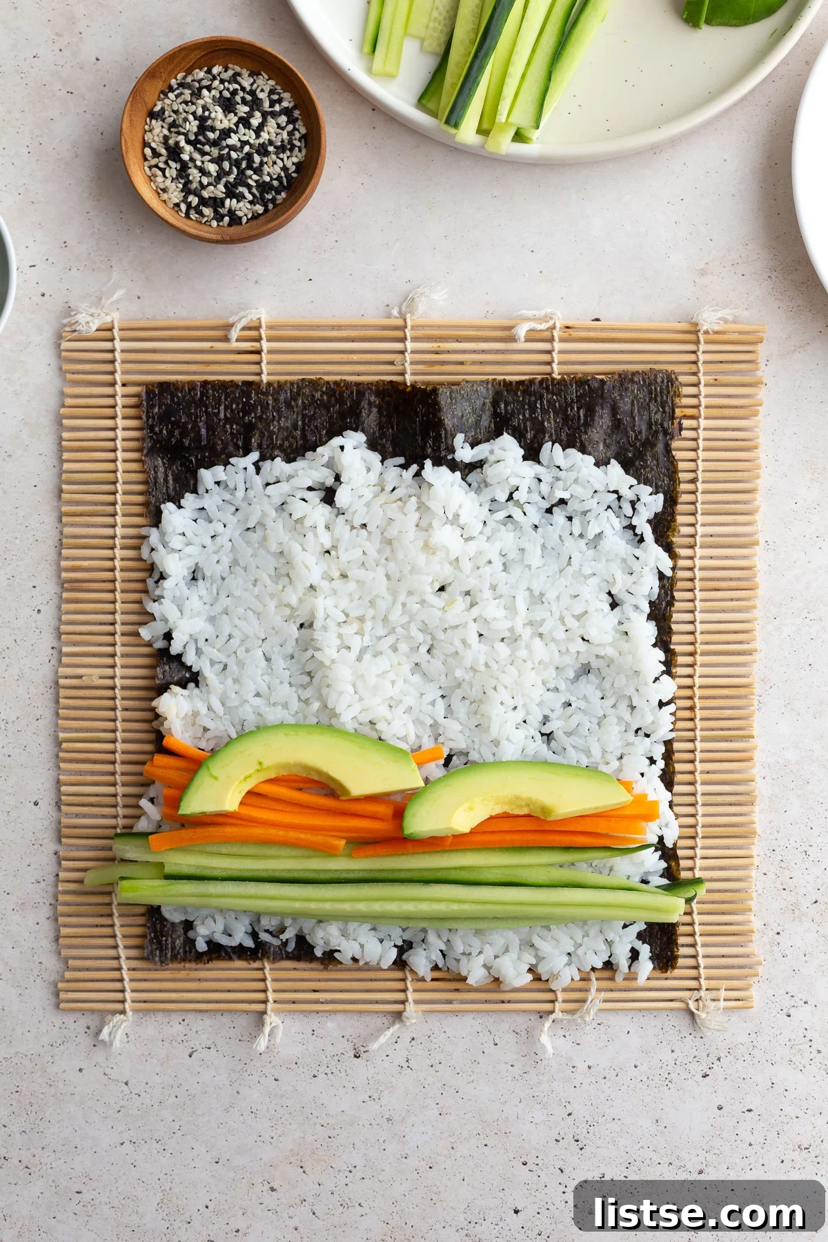 Sushi rice on a nori sheet, now topped with neat strips of vibrant pickled carrots, crisp cucumber, and creamy avocado slices.