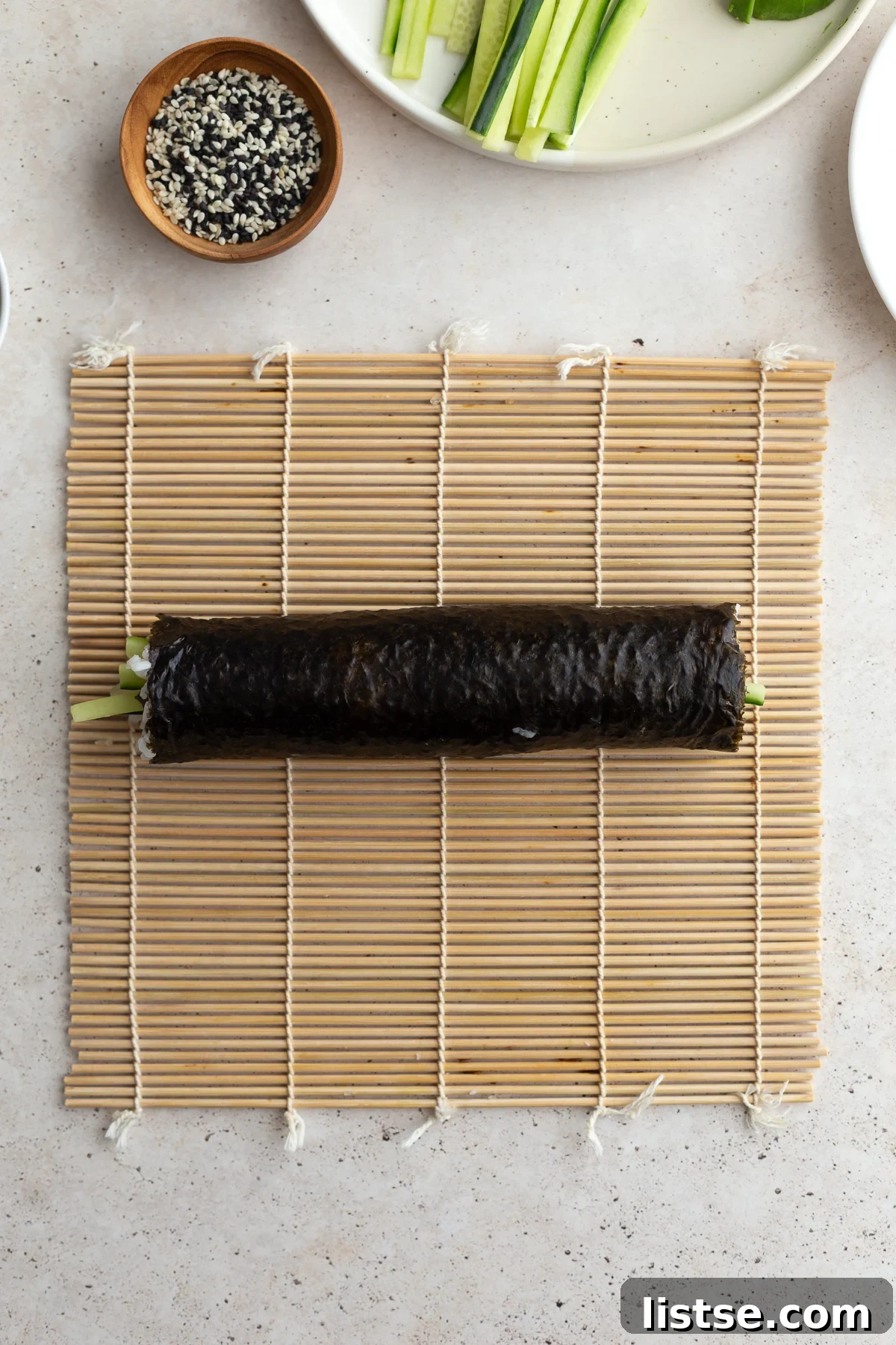 A sushi roll, tightly formed, resting on the sushi mat after being rolled up.