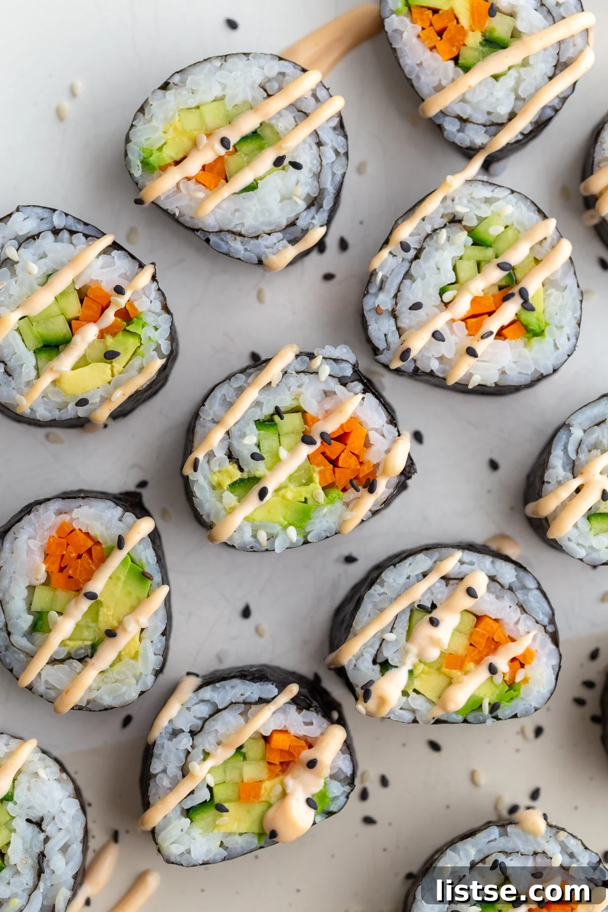 Finished cucumber rolls arranged artfully, showcasing pickled carrots, cucumber, and avocado, garnished with sesame seeds and a drizzle of spicy mayo.